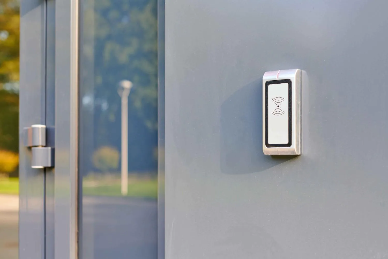 A close-up of a silver and white contactless card reader mounted on a gray door, showcasing a hardware component used in a Common Remote Doorman system for Building Security