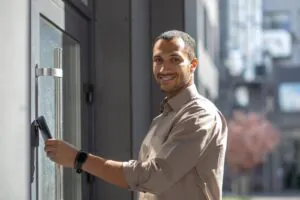 A smiling man uses his smartphone to unlock a building via an Affordable Remote Doorman system, showcasing modern Building Access Control and Virtual Doorman technology