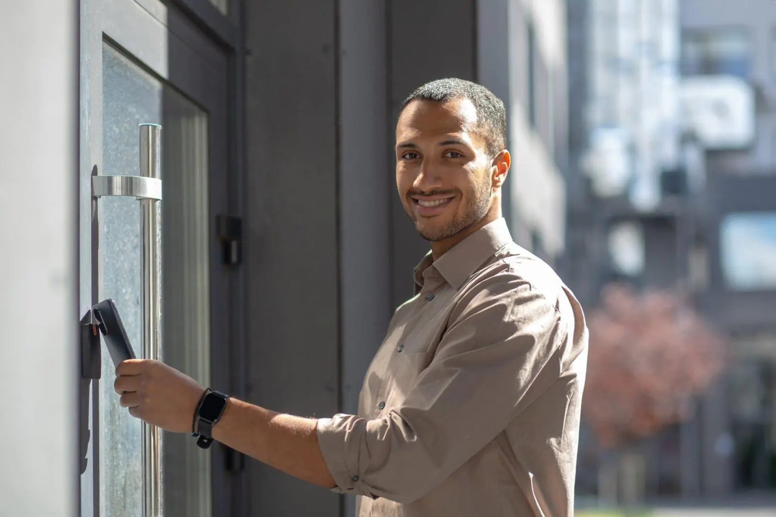 A smiling man uses his smartphone to unlock a building via an Affordable Remote Doorman system, showcasing modern Building Access Control and Virtual Doorman technology