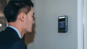 A businessman using a facial recognition wall terminal that integrates with a reliable Security Camera Monitoring Service for advanced security camera monitoring and secure live video monitoring.