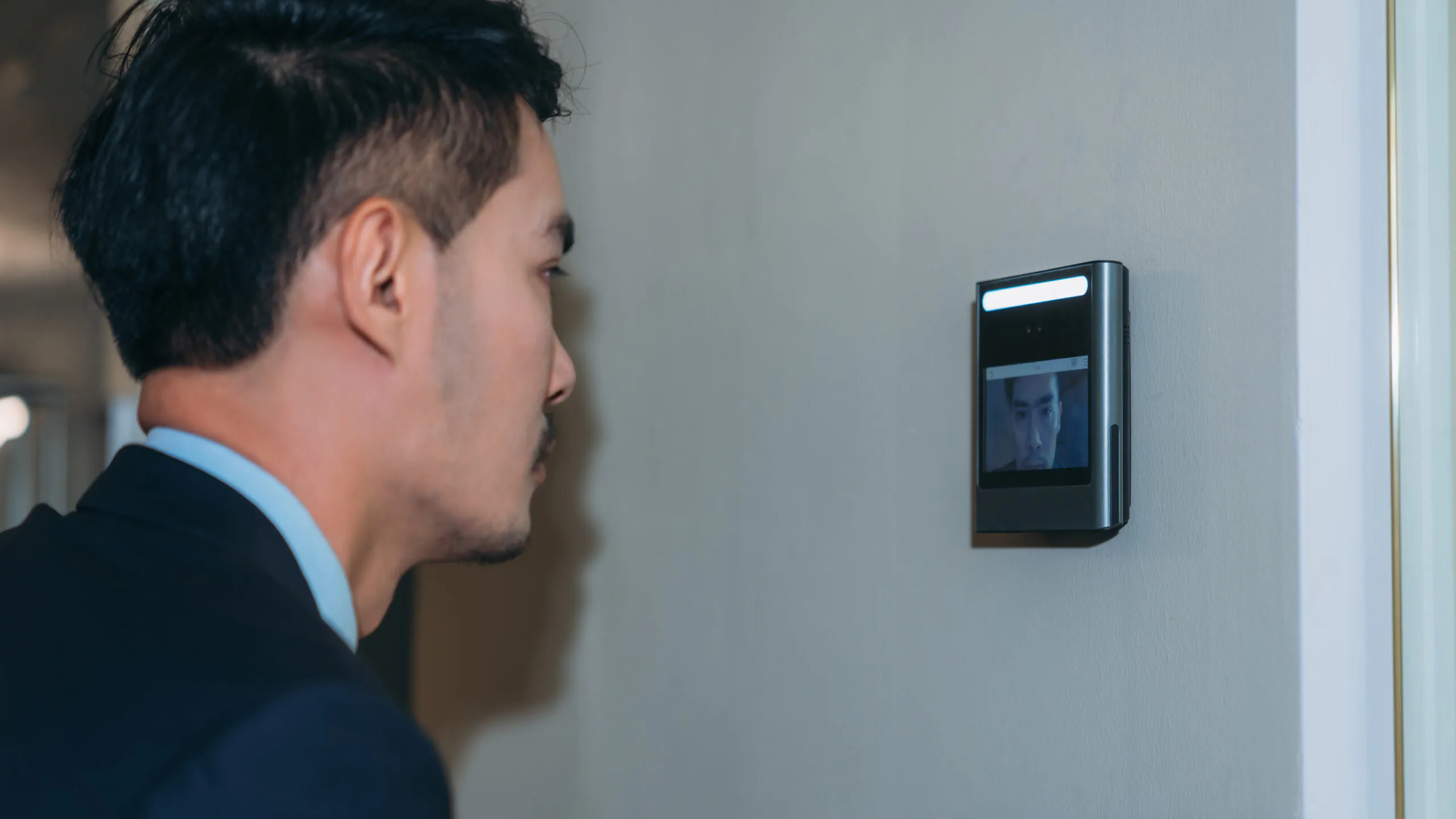 A businessman using a facial recognition wall terminal that integrates with a reliable Security Camera Monitoring Service for advanced security camera monitoring and secure live video monitoring.