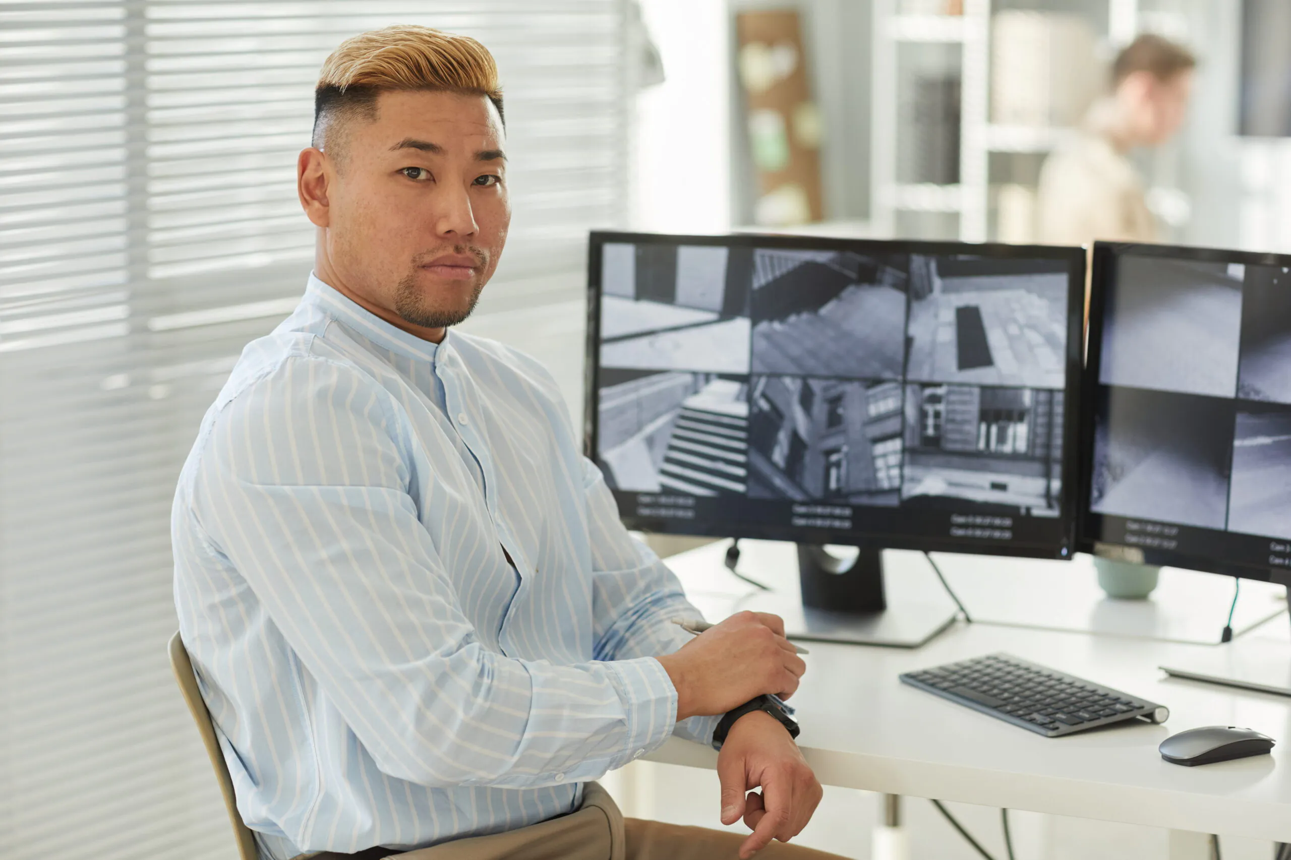 A professional Virtual Receptionist with blonde-tipped hair sitting at a desk in a bright office, monitoring building security feeds to provide elite Receptionist Services for Residential Buildings