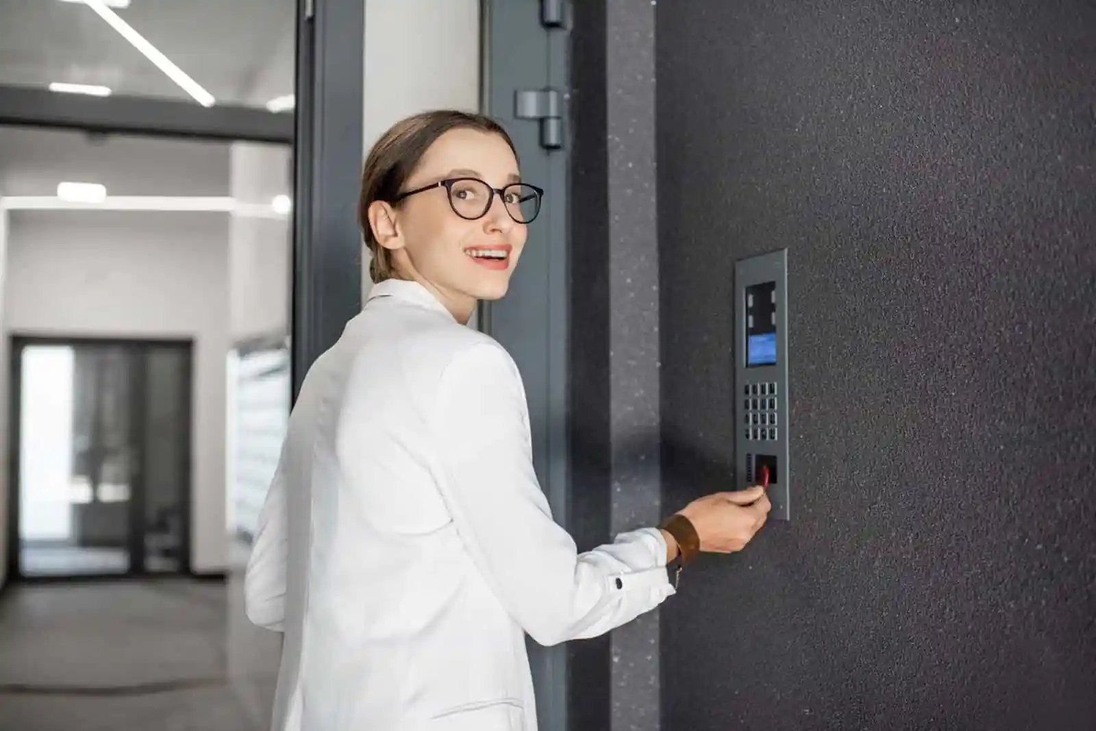 Alt Text: A smiling professional woman uses a key fob at a sleek digital access panel, demonstrating a modern Virtual Doorman for Offices system that enhances Office Security and smart Access Control.
