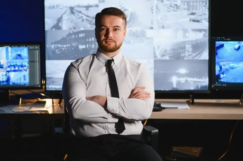 A confident professional sitting with crossed arms in a control room surrounded by high-tech Surveillance Equipment, monitoring live feeds from multiple Security Cameras to ensure a secure video surveillance system.