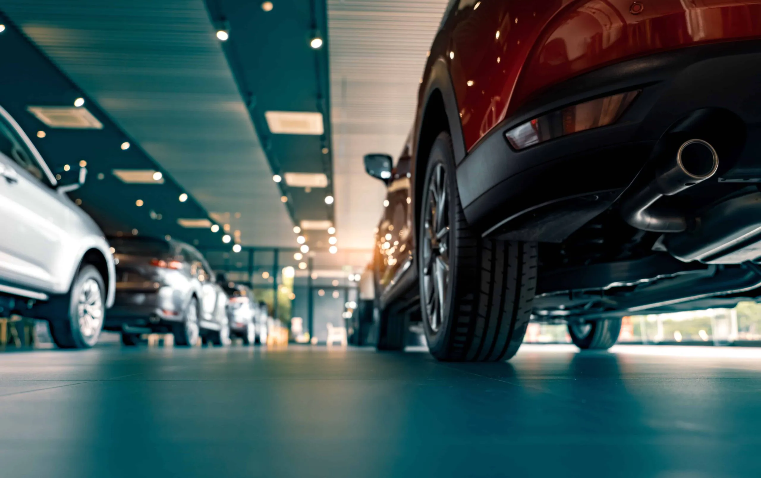 Alt Text: A low-angle view of pristine vehicles lined up inside a brightly lit showroom, demonstrating the high-value automotive inventory that requires robust CCTV Monitoring for Car Dealerships through continuous live video monitoring and a reliable security camera monitoring service.